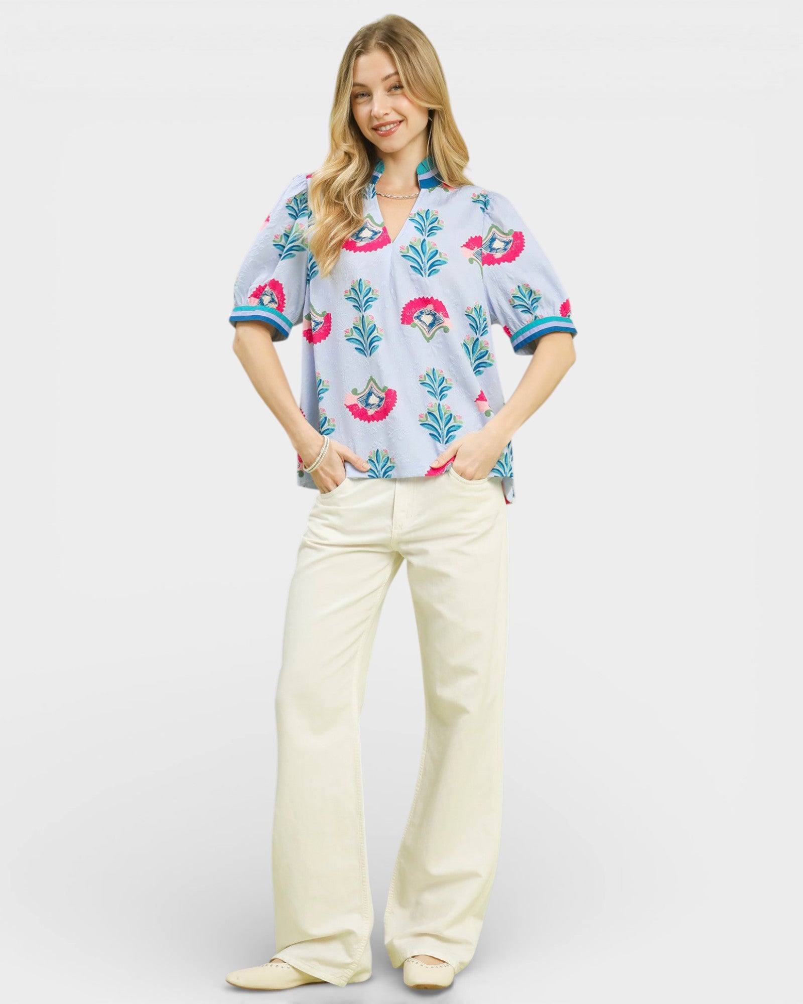 Woman wearing a colorful floral blouse and white pants on a white background