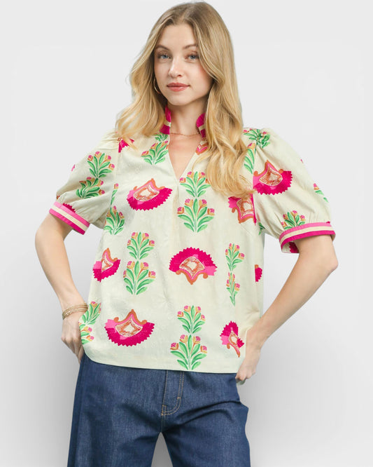 Woman wearing a floral patterned blouse with pink and green accents on a plain background