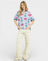 Woman wearing a colorful floral blouse and white pants on a white background