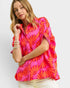 Woman wearing a bright pink and orange patterned top on a white background