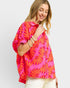 Woman wearing a bright pink and orange floral patterned top on a white background