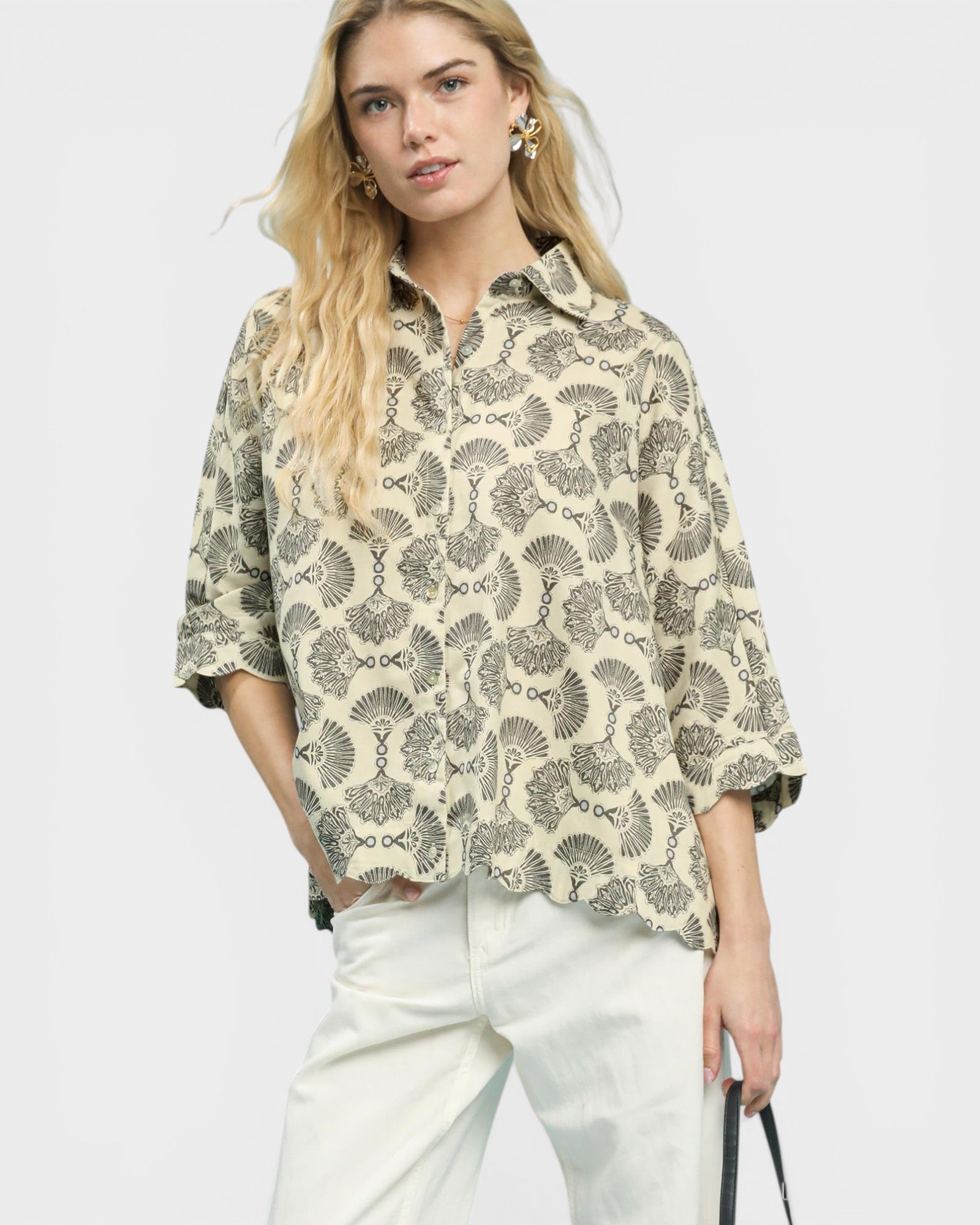 Woman wearing a patterned shirt and white pants on a plain background