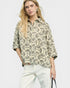 Woman wearing a patterned shirt and white pants on a plain background