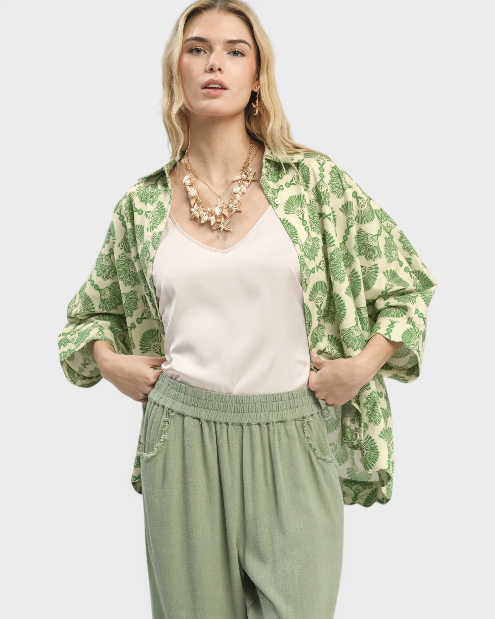 Woman wearing a green patterned jacket over a white top and green pants on a light gray background