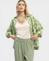 Woman wearing a green patterned jacket over a white top and green pants on a light gray background