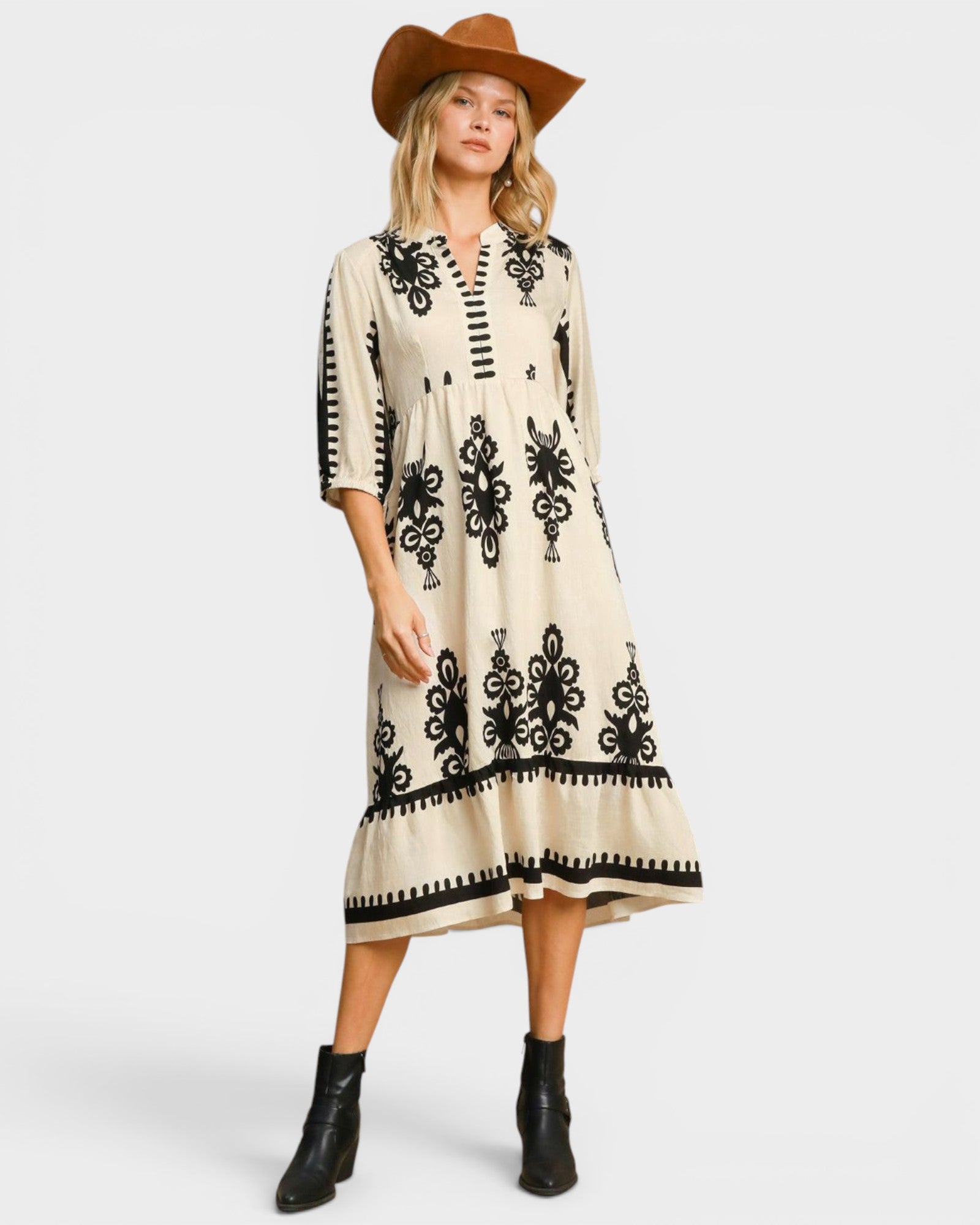 Woman wearing a cream dress with black patterns and a brown hat on a white background