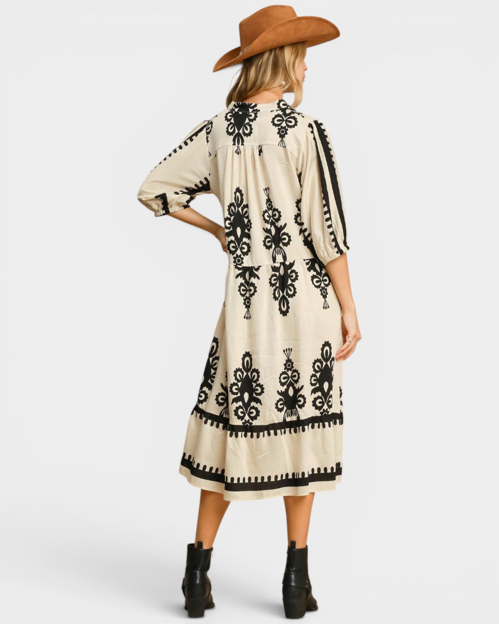 Woman wearing a cream dress with black patterns and a brown hat on a white background