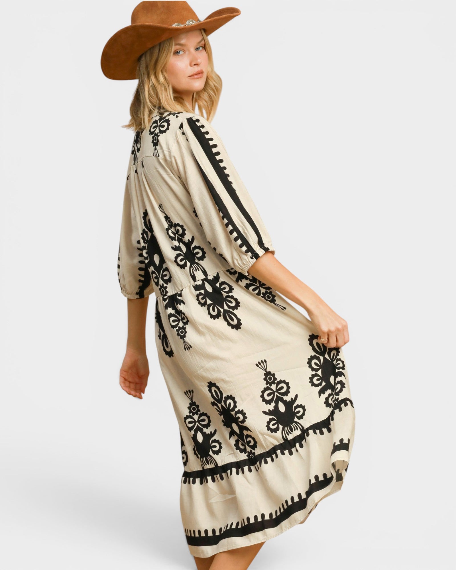 Woman wearing a beige dress with black embroidery and a brown cowboy hat on a white background