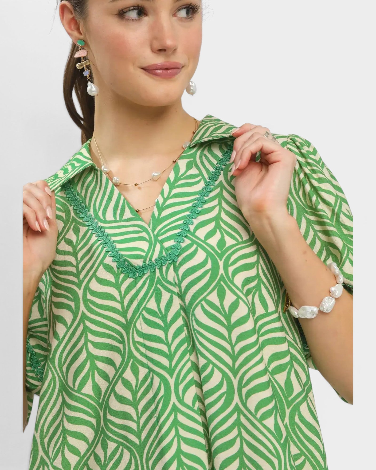 Woman wearing a green and white patterned blouse with jewelry on a plain background