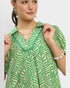 Woman wearing a green and white patterned blouse with jewelry on a plain background