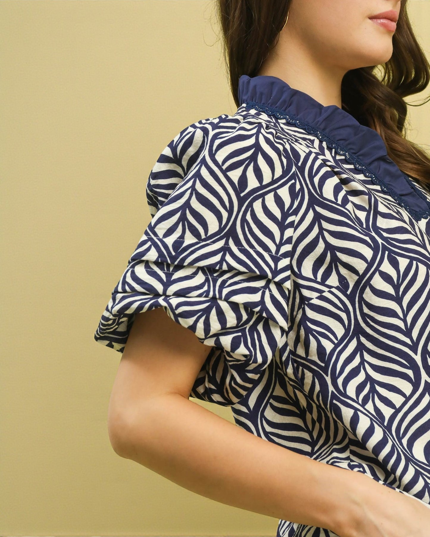 Close-up of a person wearing a navy and white patterned blouse against a beige background