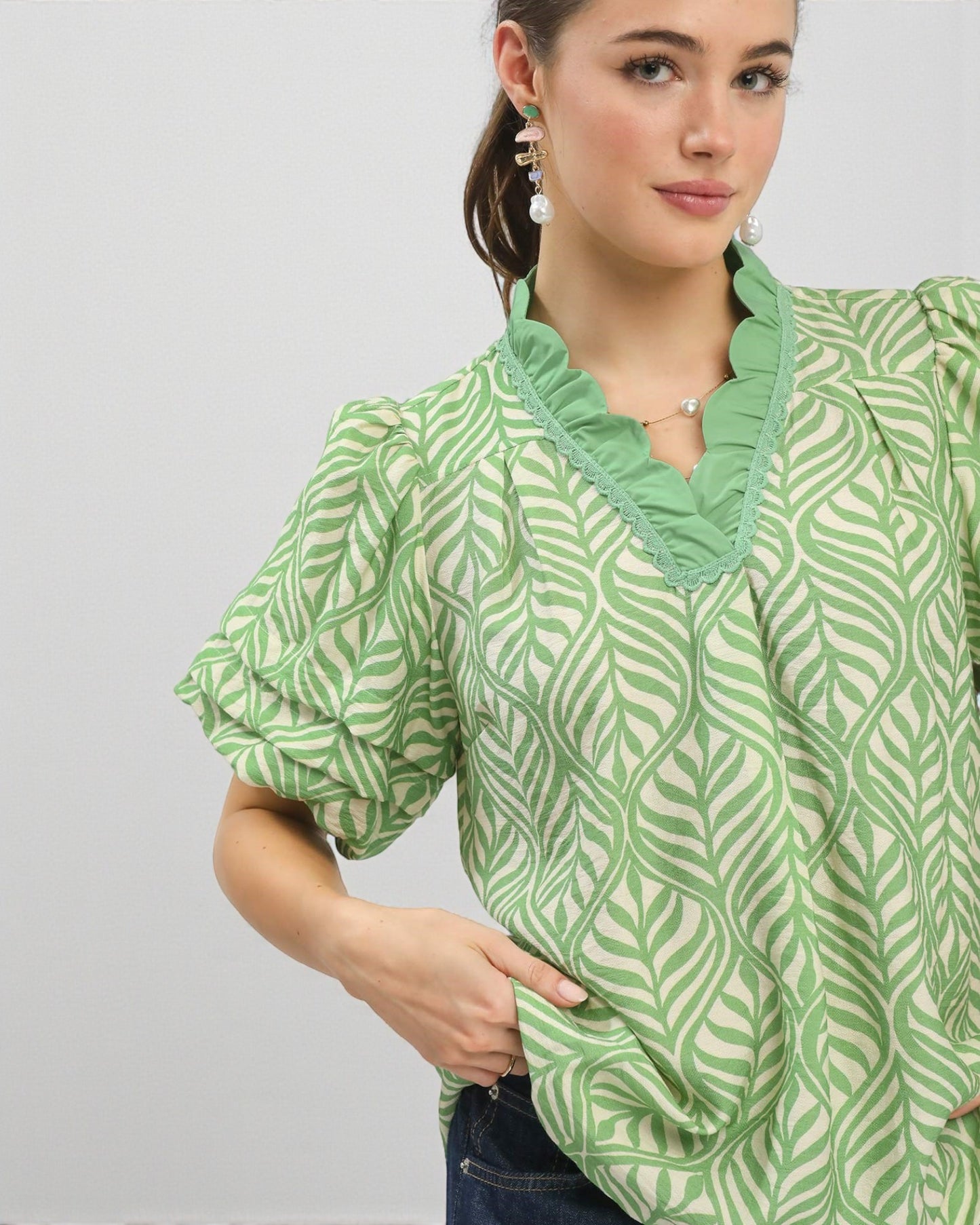 Woman wearing a green patterned blouse against a light gray background