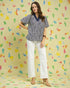 Woman wearing a patterned blouse and white pants against a colorful abstract background