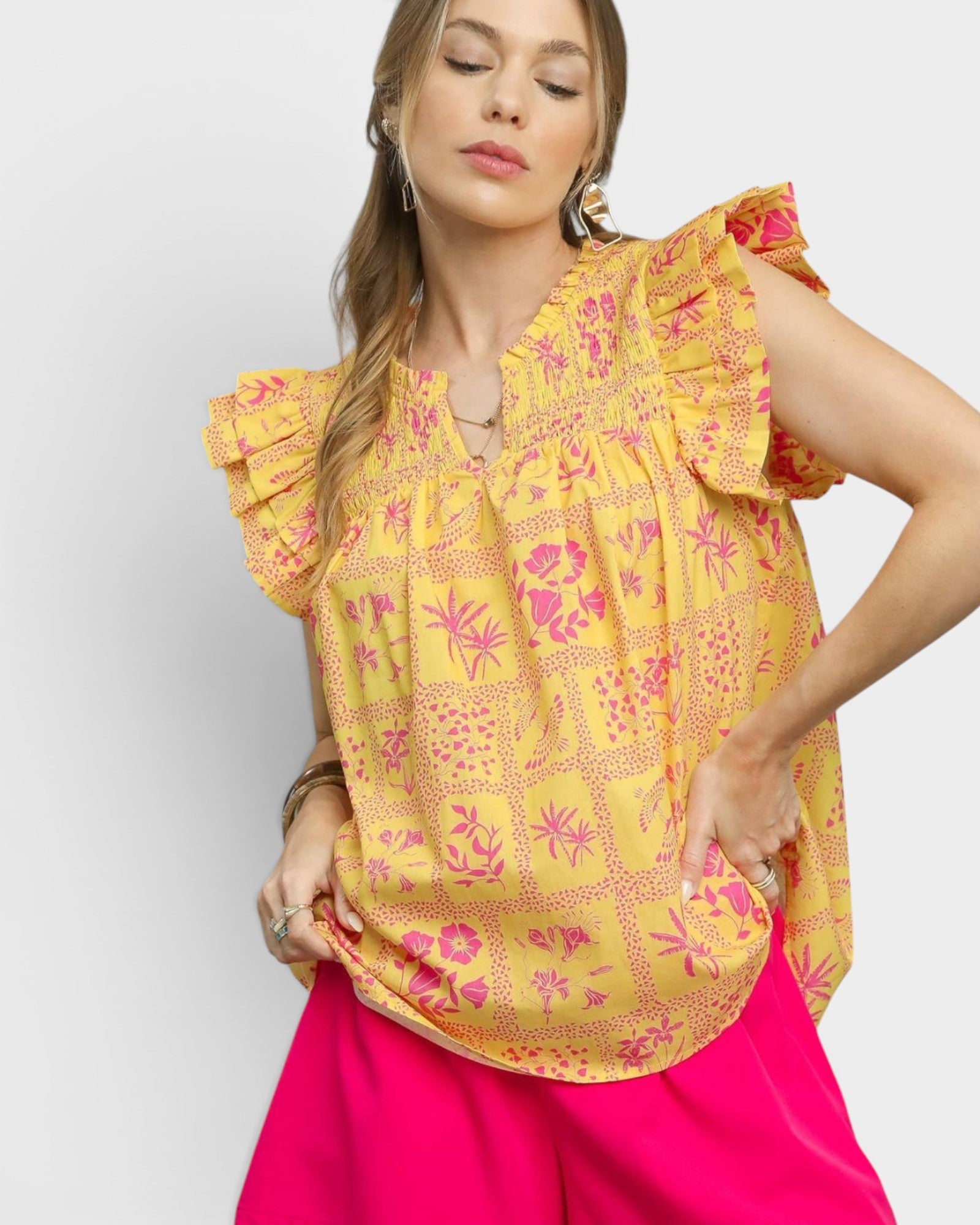 Woman wearing a yellow floral blouse with pink pants on a light gray background