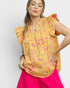 Woman wearing a yellow floral blouse with pink pants on a light gray background