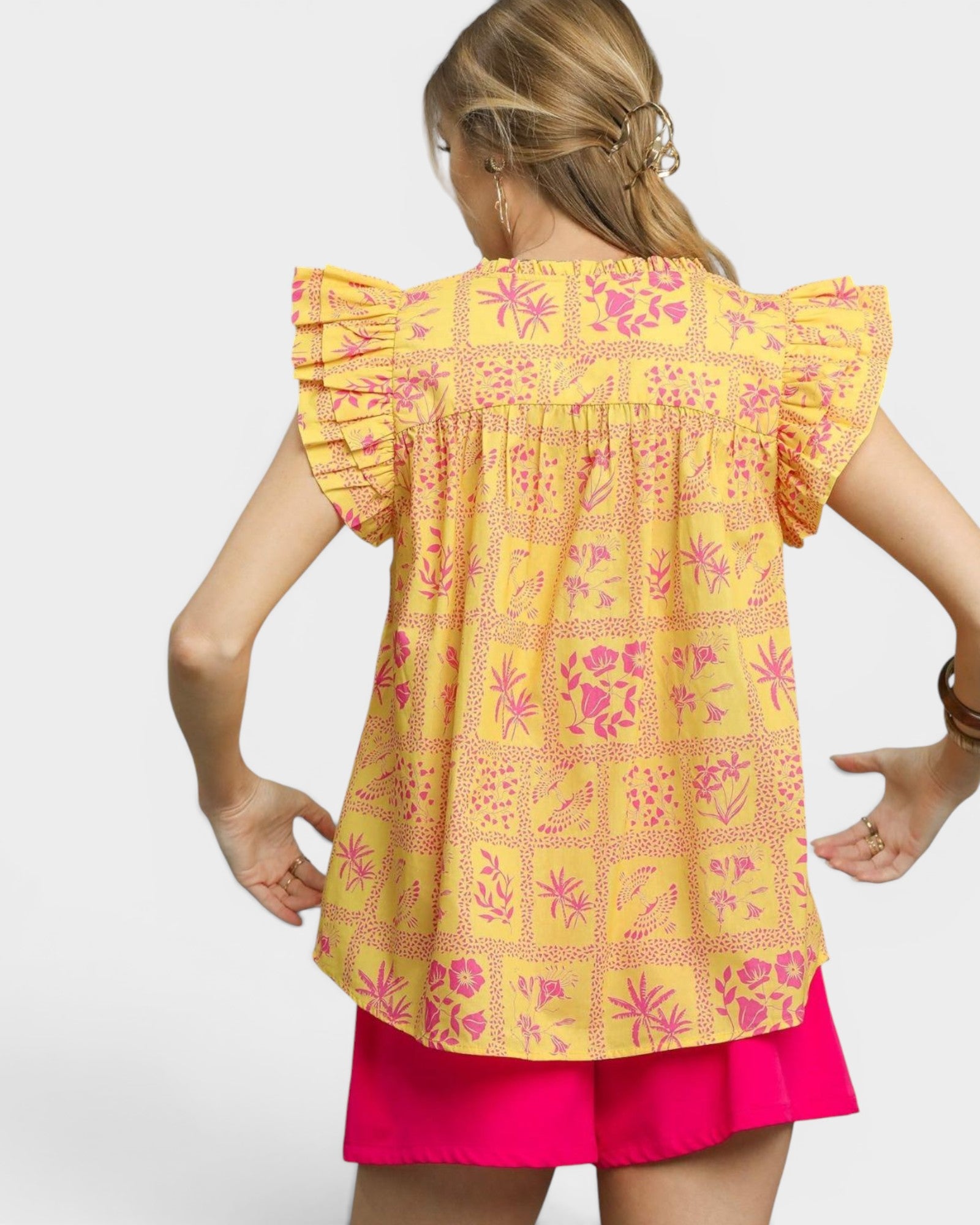 Woman wearing a yellow and pink patterned top with ruffled sleeves on a white background