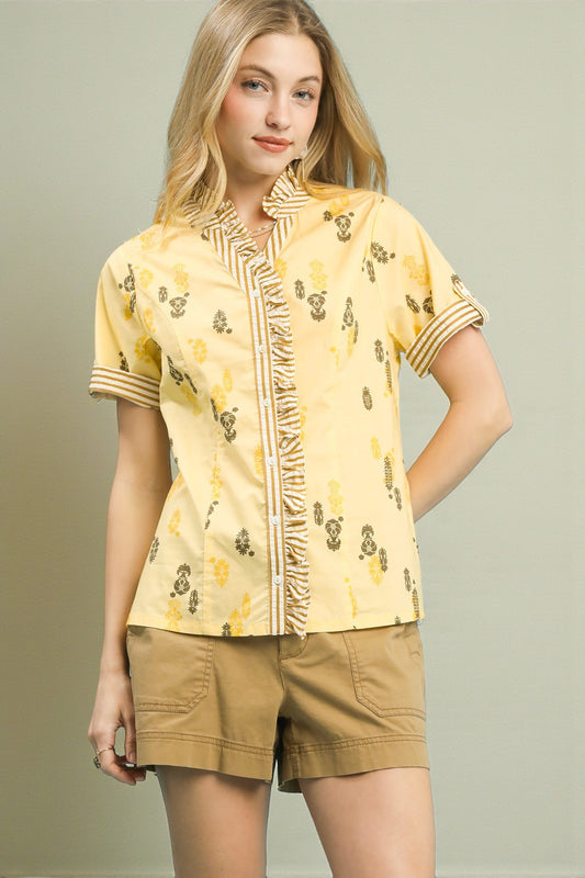 Woman wearing a yellow patterned shirt and beige shorts against a plain background