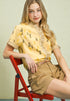 Woman sitting on a red chair wearing a yellow blouse with floral patterns and beige shorts.