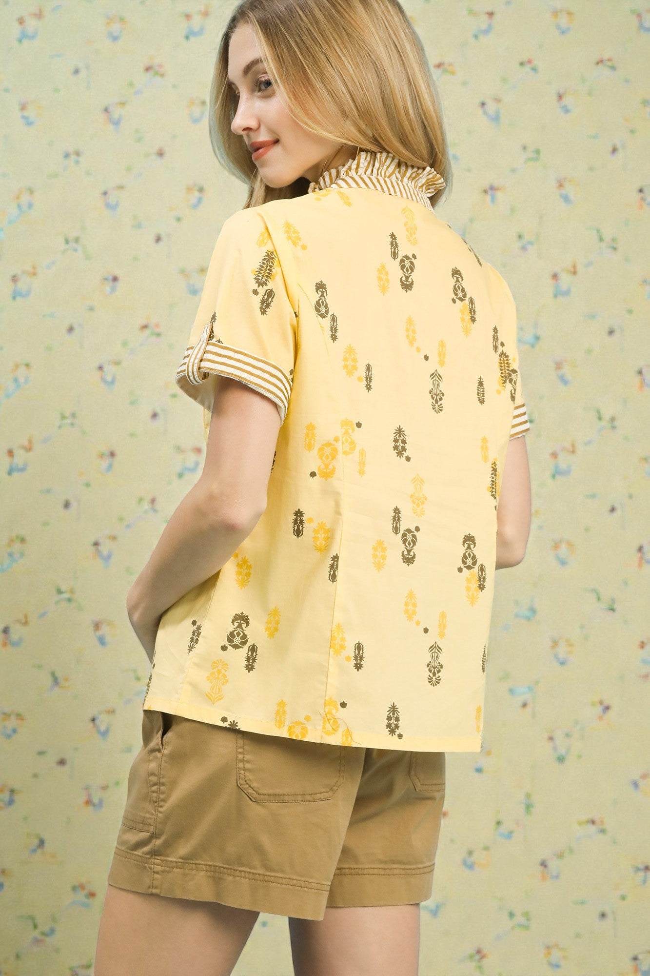 Woman wearing a yellow patterned shirt and beige shorts against a light background