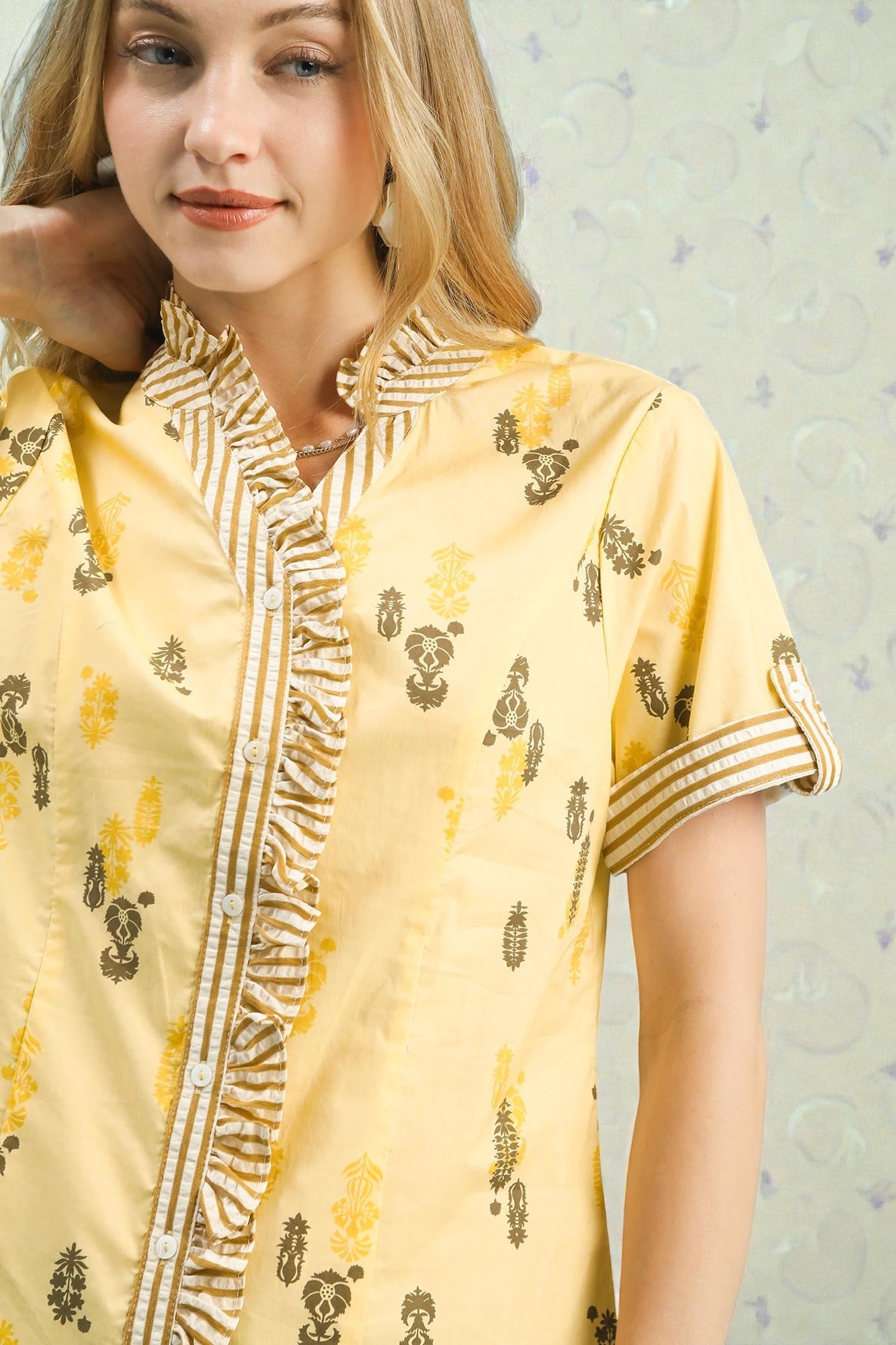 Woman wearing a yellow traditional outfit with intricate patterns against a light background
