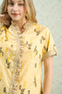 Woman wearing a yellow traditional outfit with intricate patterns against a light background