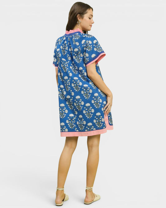 Woman wearing a blue patterned dress with pink trim on a white background