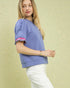 Woman wearing a purple blouse with ruffled sleeves against a light green background
