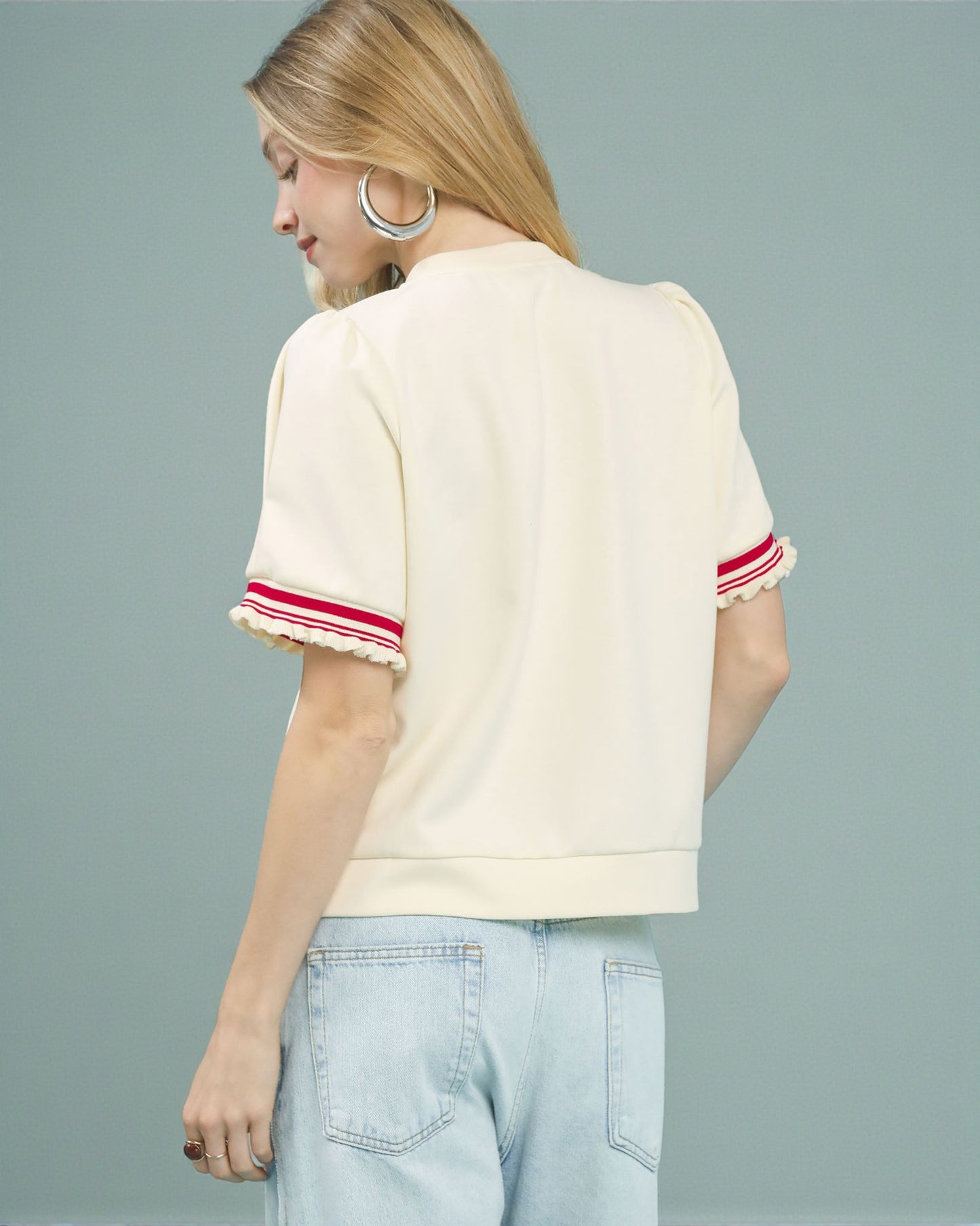 Woman wearing a cream-colored top with red trim on a gray background