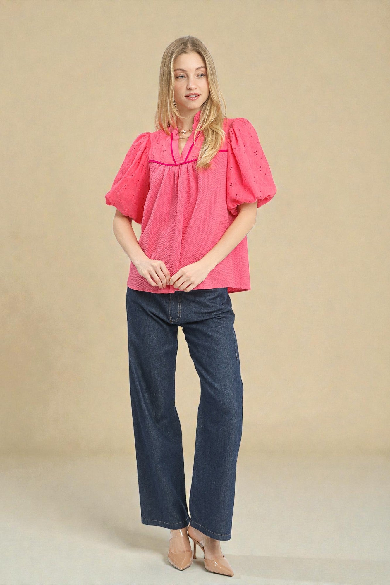Woman wearing a pink blouse and blue jeans against a beige background