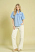 Woman wearing a light blue blouse and white pants against a beige background
