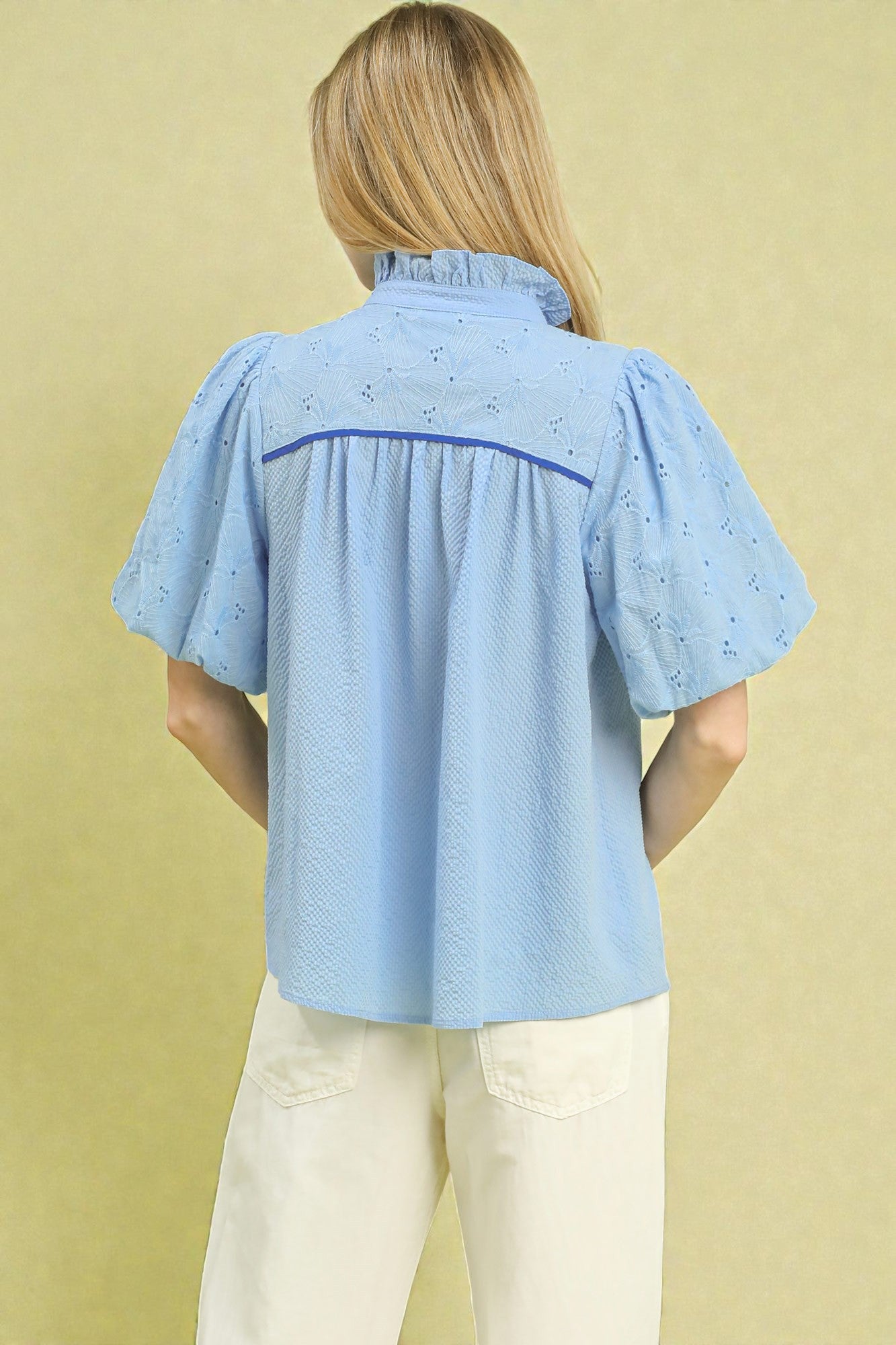 Woman wearing a light blue blouse with a subtle pattern against a beige background