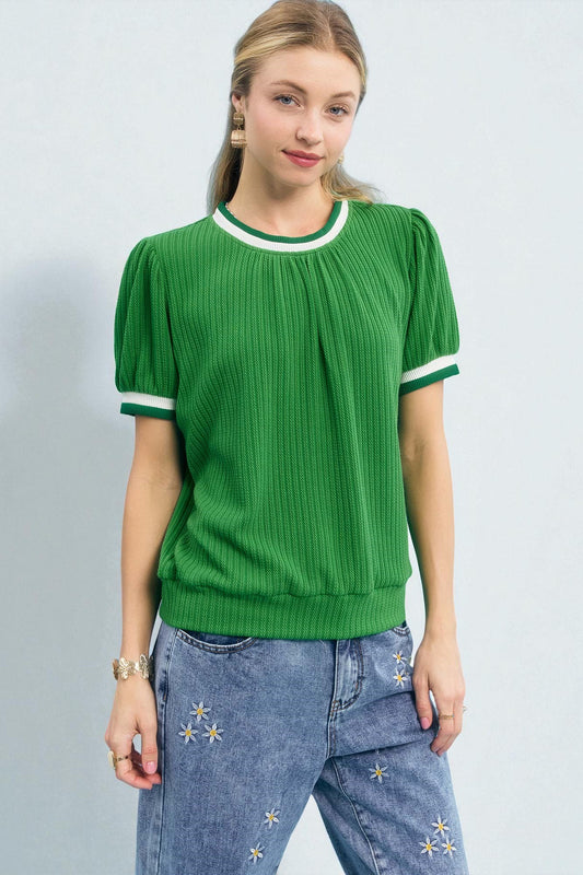 Woman wearing a green ribbed sweater with white trim and blue jeans on a light gray background