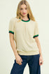 Woman wearing a cream-colored sweater with green trim on a beige background