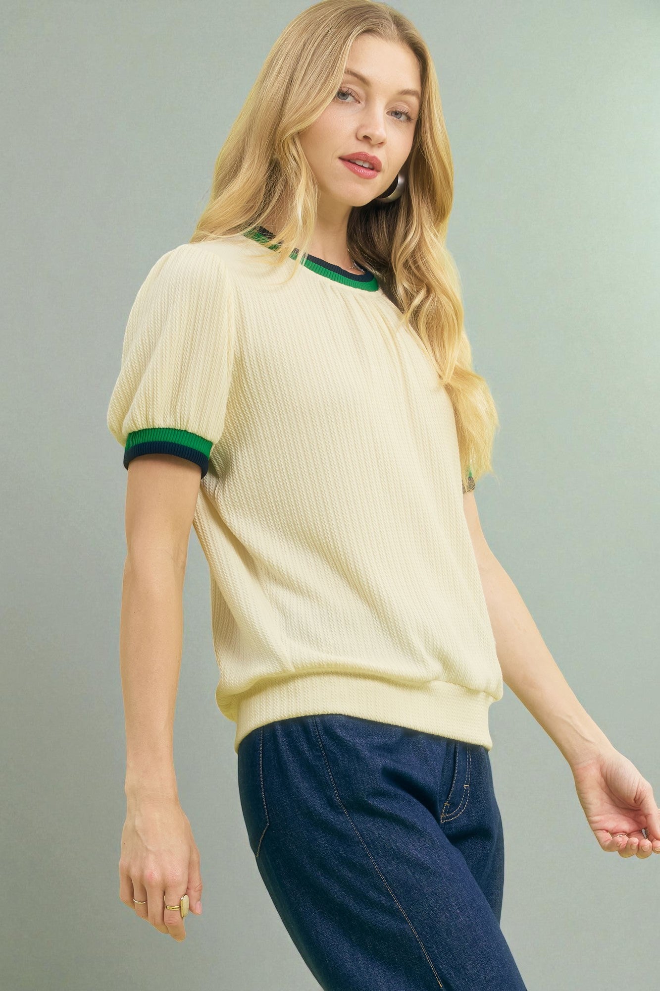 Woman wearing a light yellow sweater with green trim on a gray background
