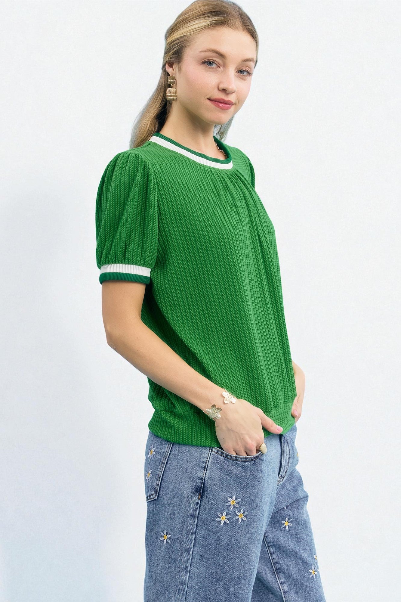 Woman wearing a green ribbed sweater with white trim on a white background