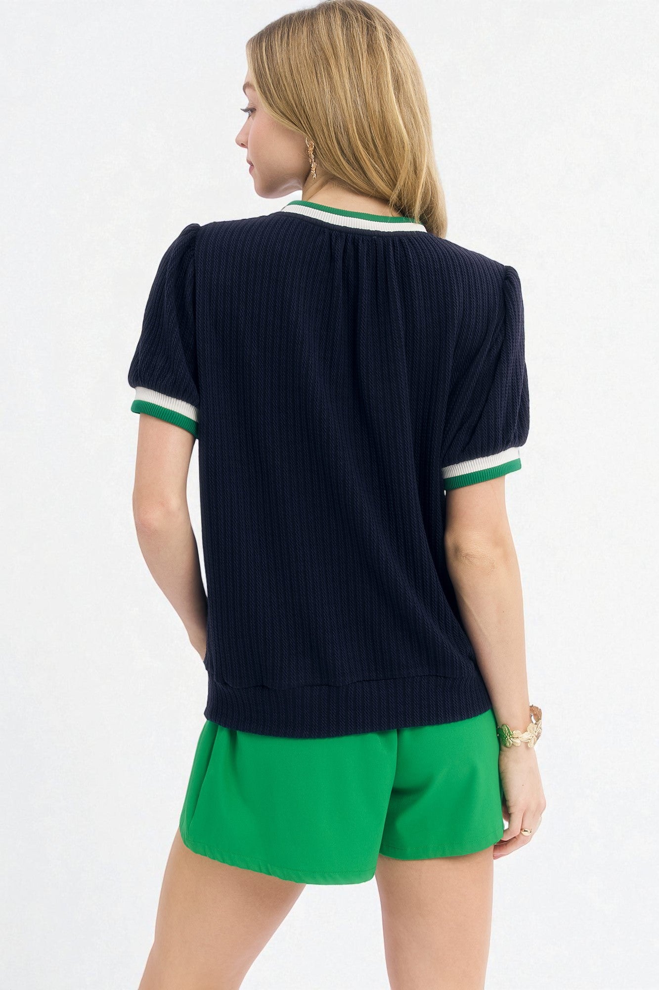 Woman wearing a navy sweater with green trim and green shorts on a white background