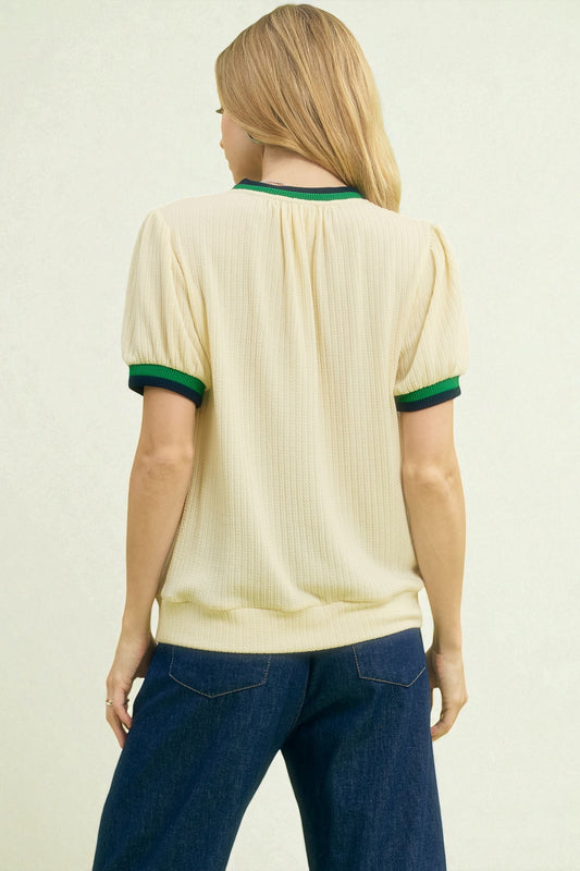 Person wearing a cream-colored shirt with green trim on a plain background