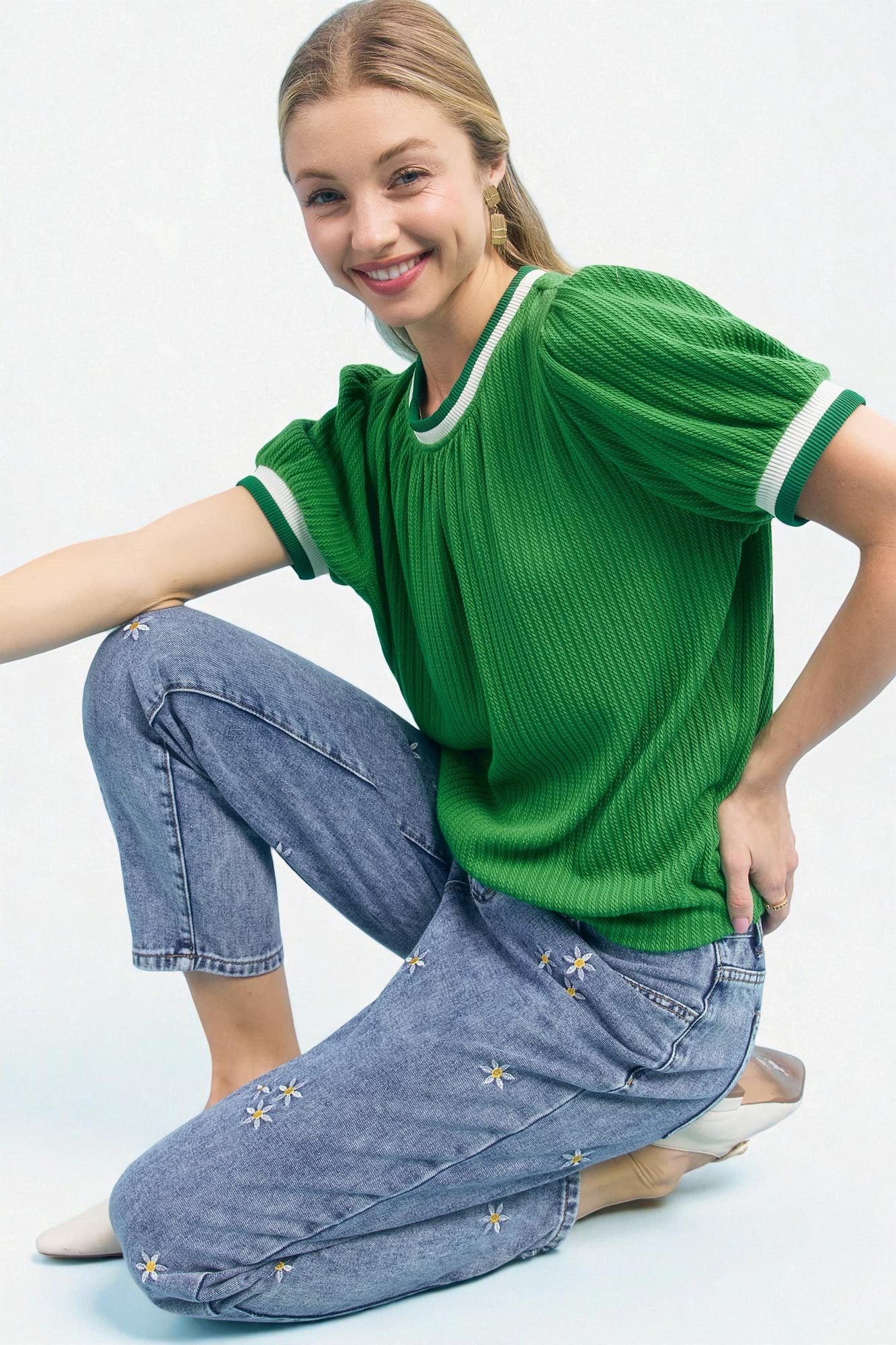 Woman wearing a green ribbed sweater and blue jeans with star patterns on a white background
