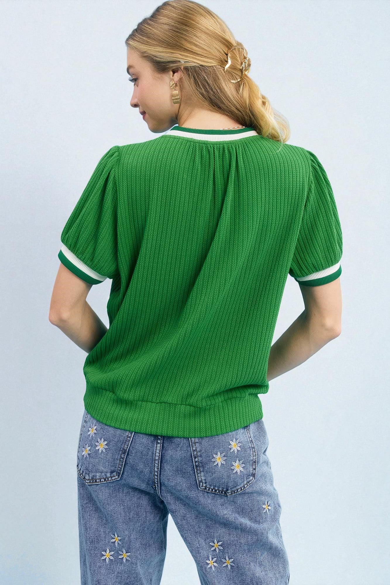 Person wearing a green ribbed sweater and blue jeans with star patterns on a light gray background