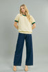 Woman wearing a yellow blouse with green trim and blue jeans on a gray background