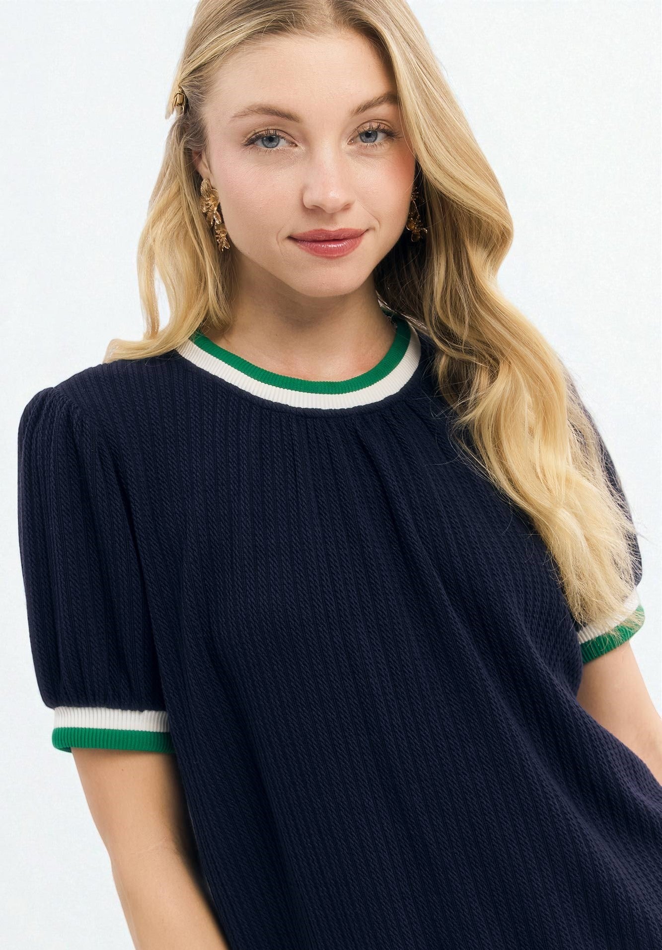 Woman wearing a navy blue dress with green and white trim on a white background