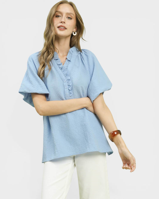 Woman wearing a light blue blouse and white pants on a plain background