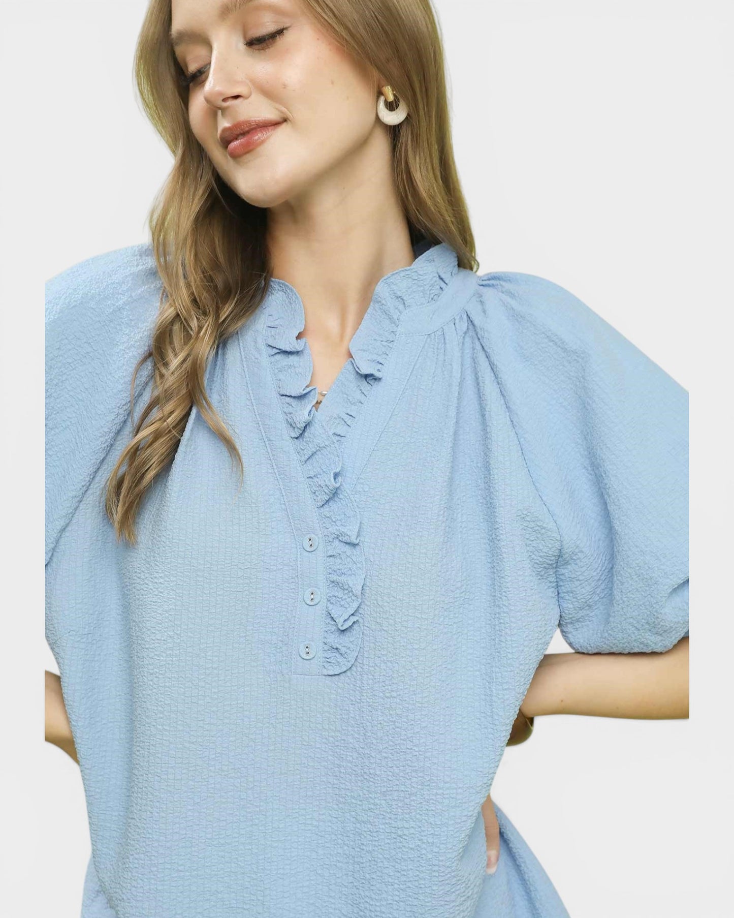 Woman wearing a light blue dress with ruffled details on a plain background