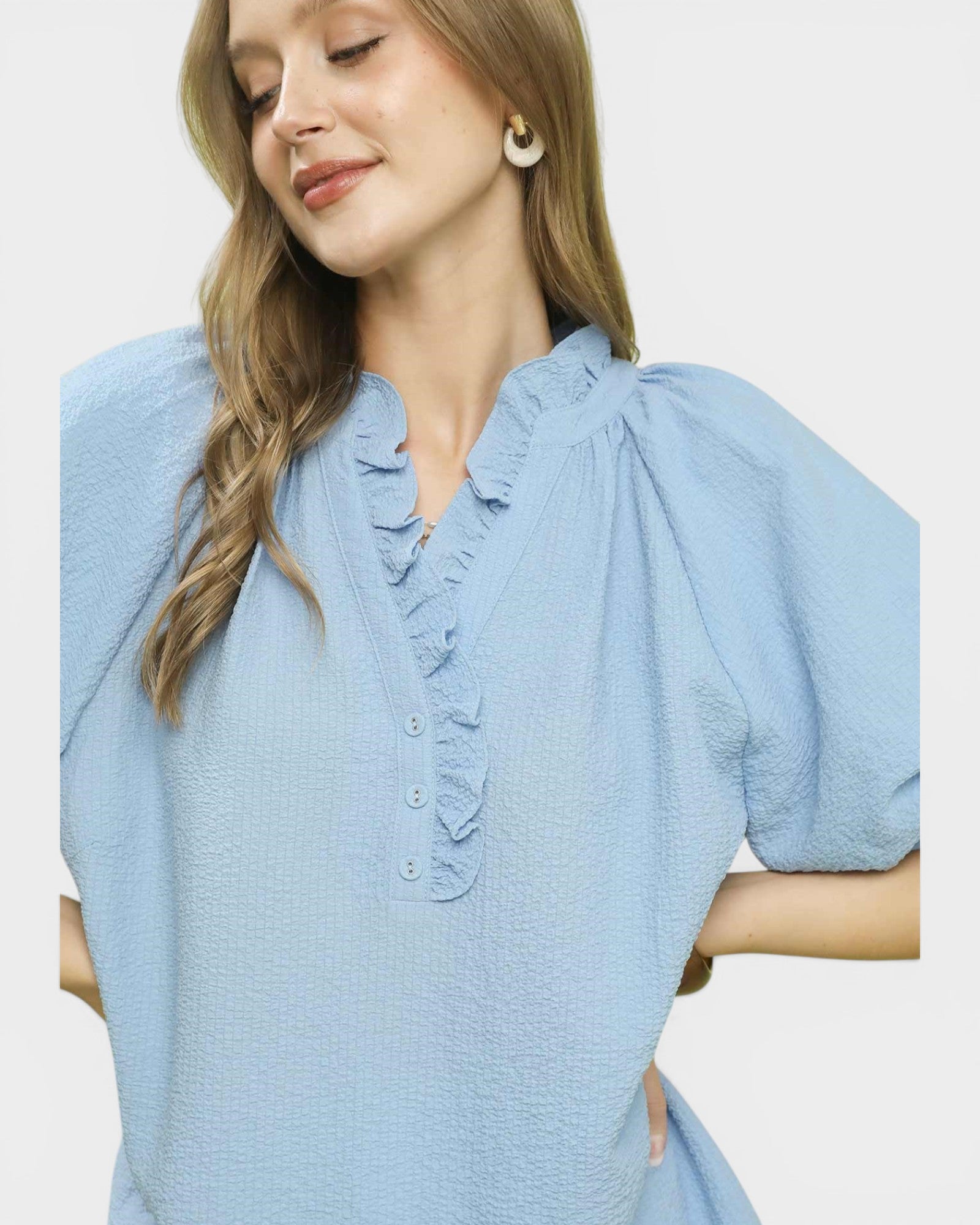 Woman wearing a light blue dress with ruffled details on a plain background