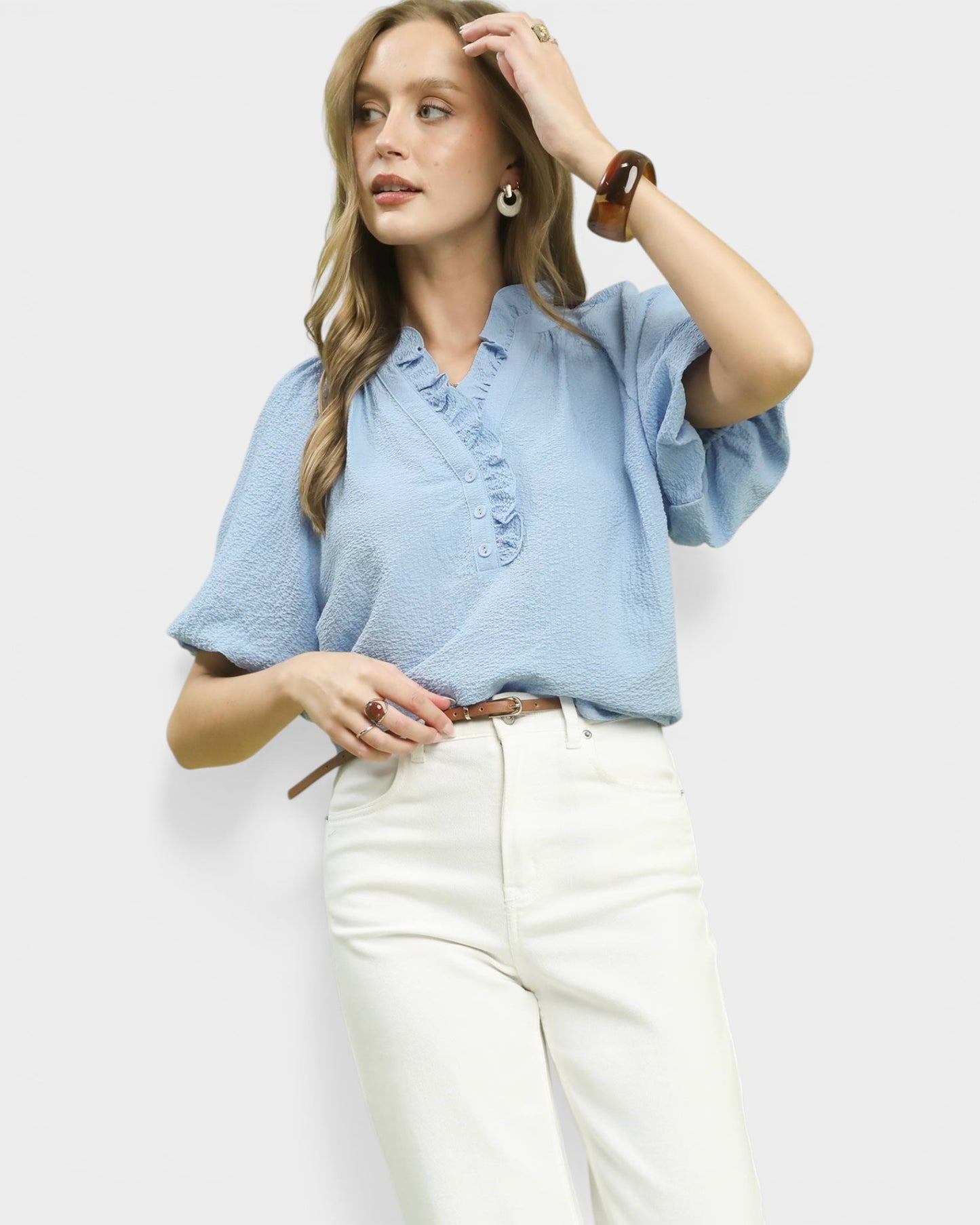 Woman wearing a light blue blouse and white pants against a plain background