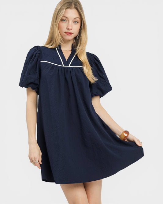 Woman wearing a navy blue dress with white trim on a plain background