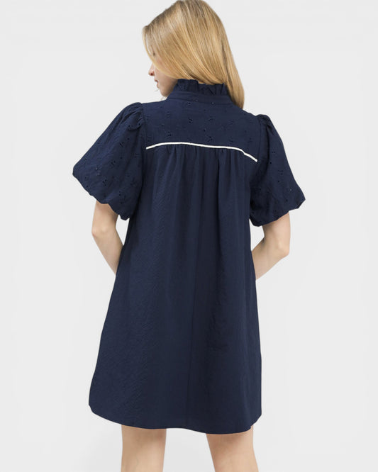 Woman wearing a navy dress with white trim on a light gray background