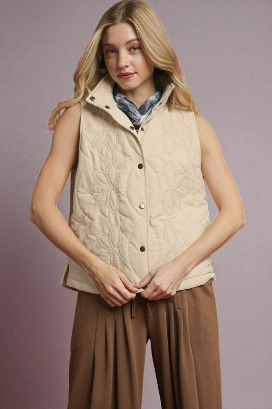 Woman wearing a beige quilted vest over a patterned scarf with a plain background