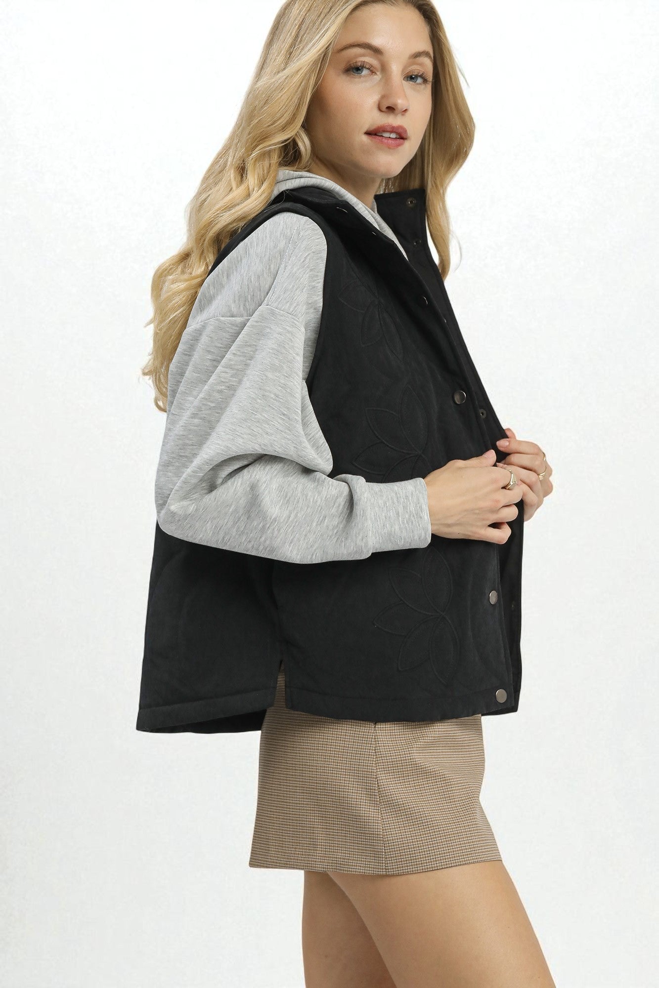 Woman wearing a black vest over a gray shirt with a white background