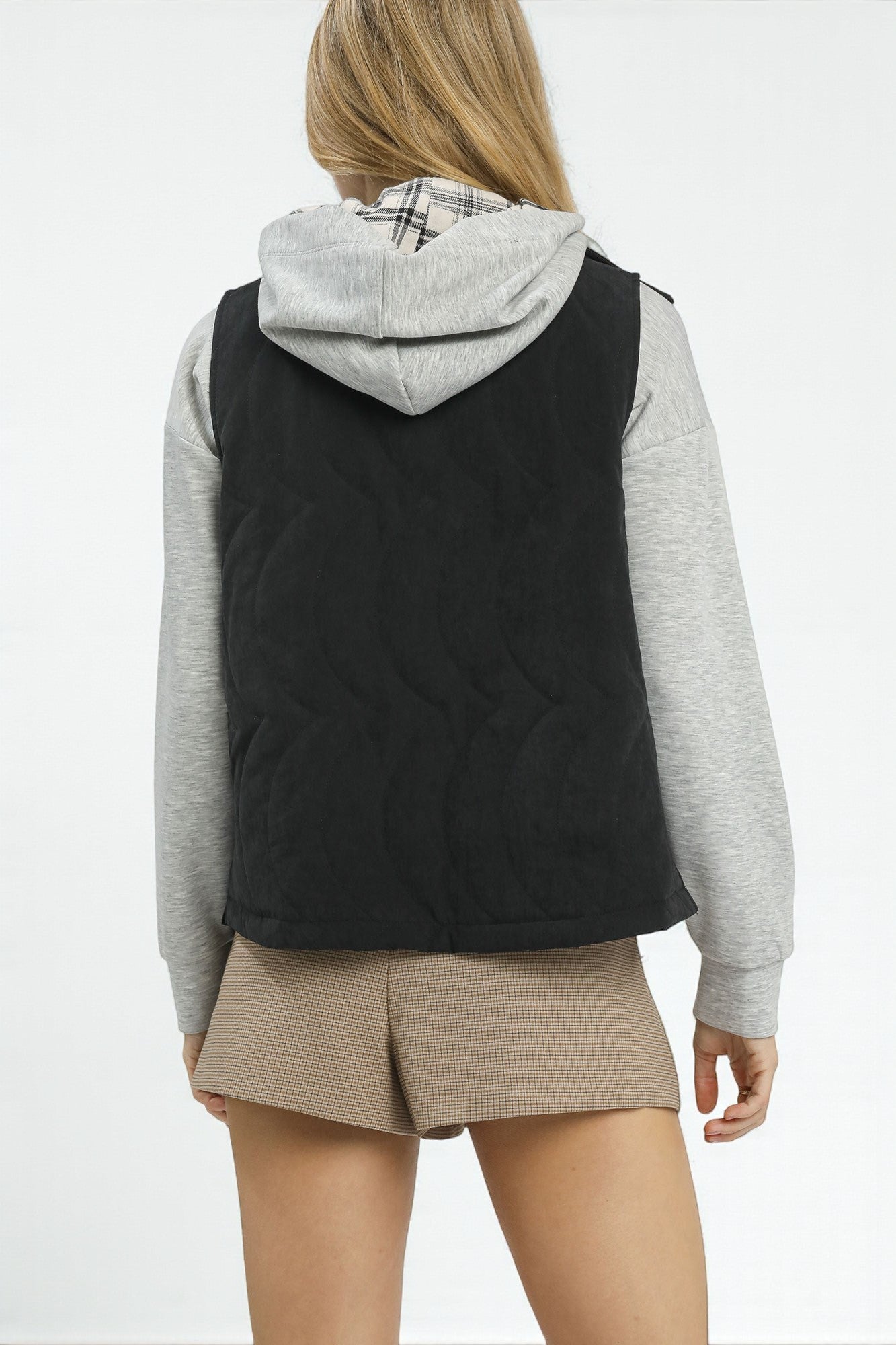 Person wearing a black quilted vest over a gray hoodie on a white background